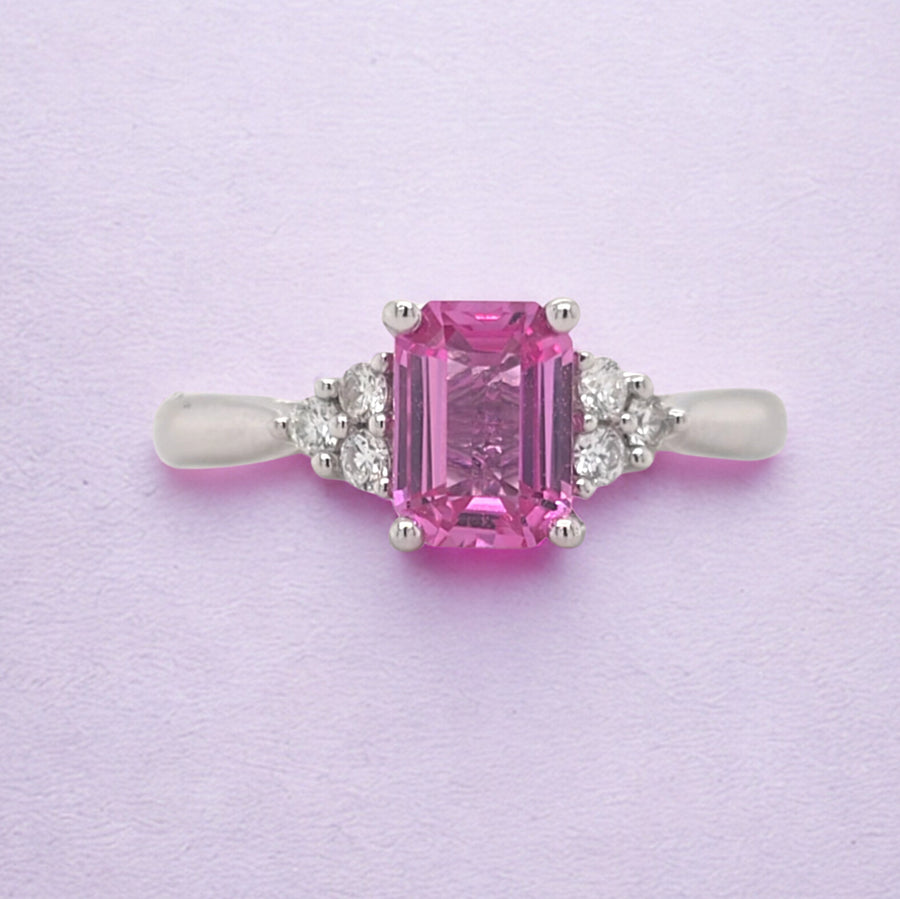 18ct white gold ring with an octagon pink sapphire flanked by trios of diamonds on each shoulder, on lilac background